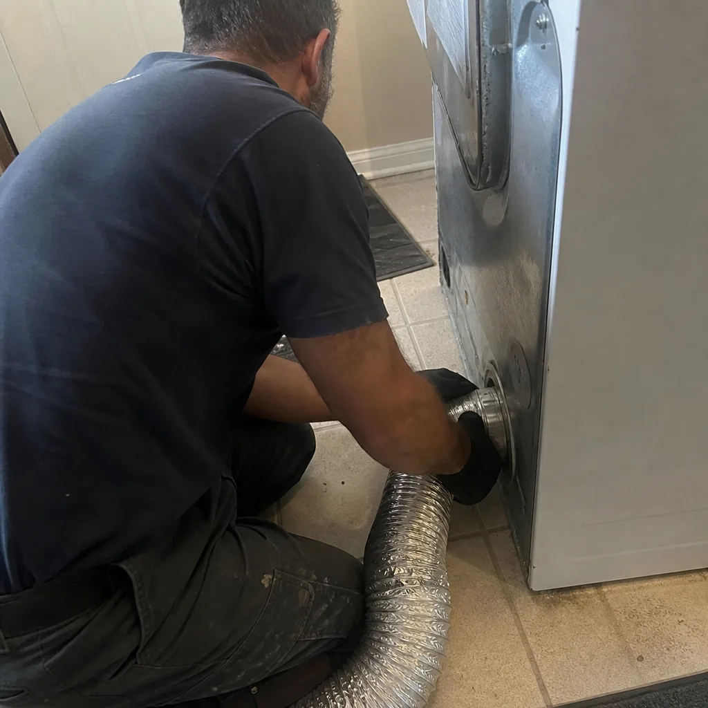 Technician attaching a silver flexible dryer vent hose to a dryer
